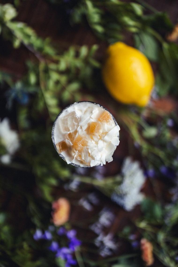 Cocktail med sukkerkant set ovenfra, omgivet af citron, urter og blomster