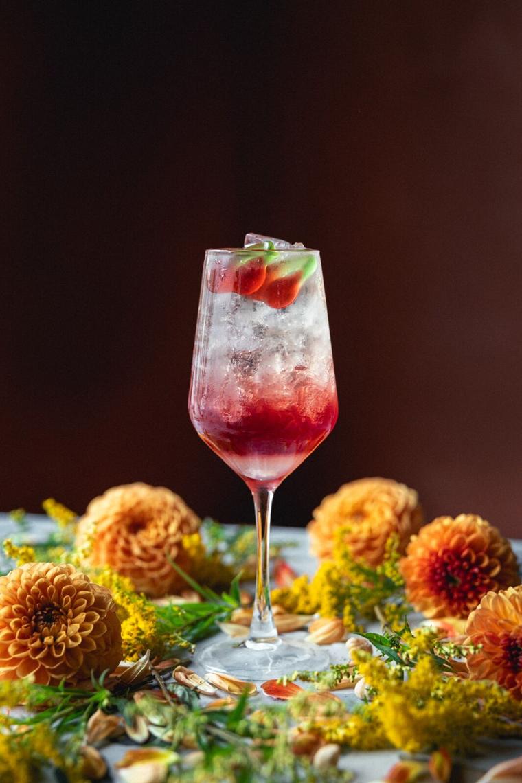 Rød spritz i vinglas med jordbær og is mellem orange dahliaer